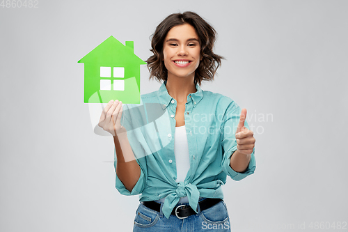 Image of smiling woman with green house showing thumbs up