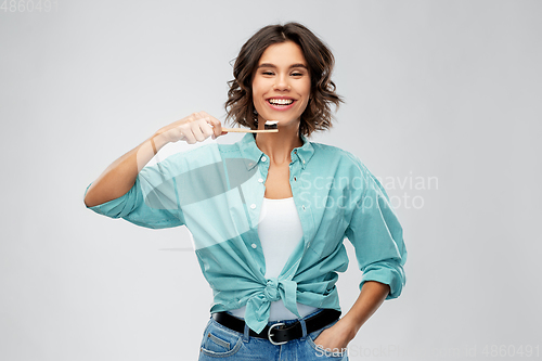 Image of smiling woman with toothpaste on wooden toothbrush