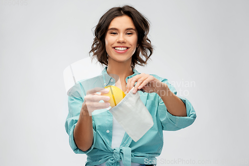 Image of happy woman putting orange into reusable bag