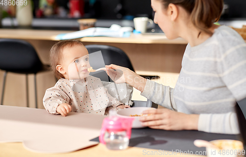 Image of happy mother feeding baby with puree at home