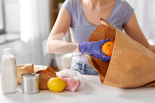 Image of woman in gloves taking food from paper bag at home