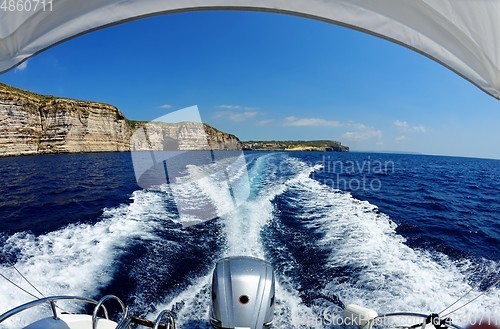Image of Fisheye view of the powerboat stern trail on sea water and the cliffs of Gozo island in Malta in bright day