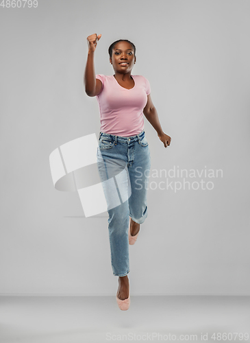 Image of happy african american woman jumping over grey