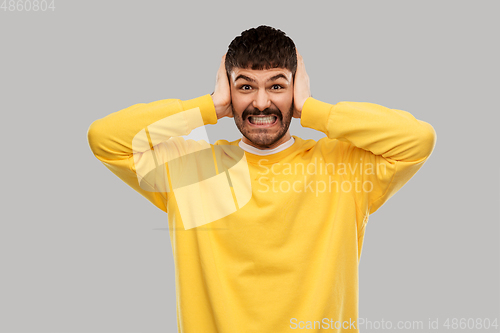 Image of man in yellow sweatshirt closing ears by hands