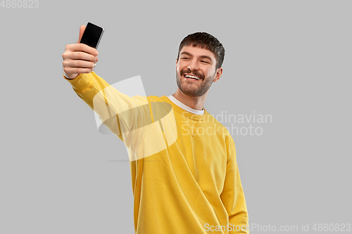 Image of smiling young man taking selfie with smartphone