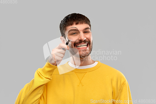 Image of smiling man in yellow sweatshirt with magnifier