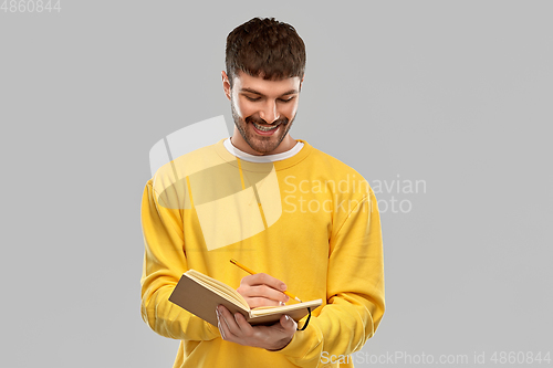 Image of smiling man in yellow sweatshirt writing to diary