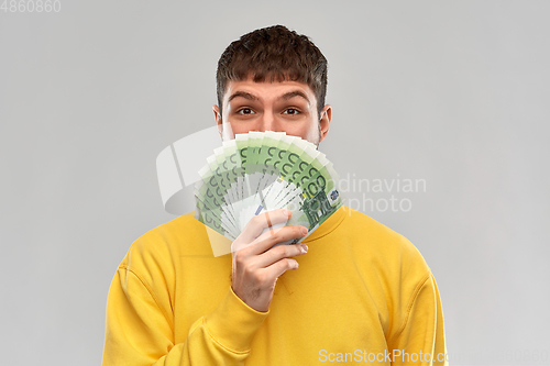 Image of happy young man in yellow sweatshirt with money