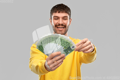 Image of smiling young man in yellow sweatshirt with money