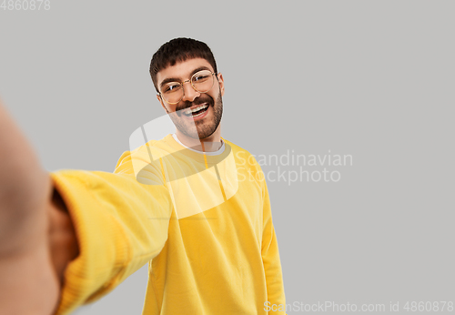 Image of happy young man in yellow sweatshirt making selfie