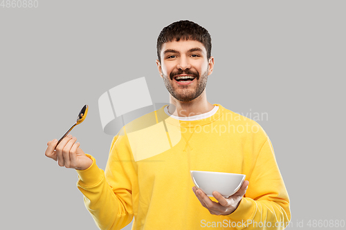 Image of smiling young man with spoon and bowl eating