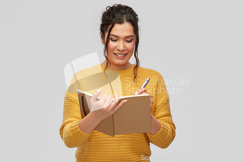 Image of happy young woman writing to diary or notebook