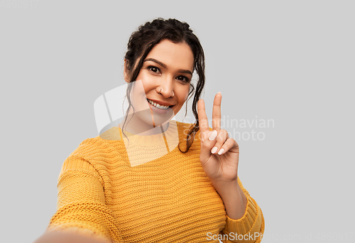Image of woman with pierced nose taking selfie shows peace