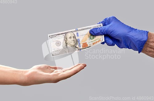 Image of one hand in medical glove giving money to another