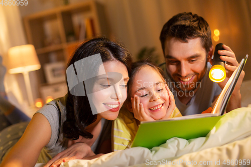 Image of happy family reading book in bed at night at home