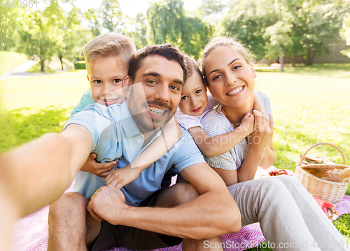 Image of family having picnic and taking selfie at park