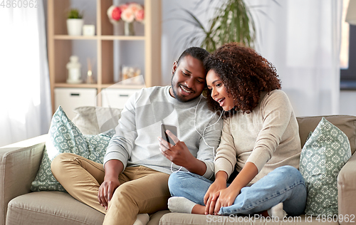 Image of happy couple with smartphone and earphones at home