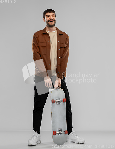 Image of smiling young man in brown jacket with skateboard