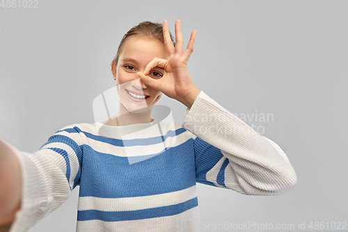 Image of smiling teenage girl in pullover taking selfie