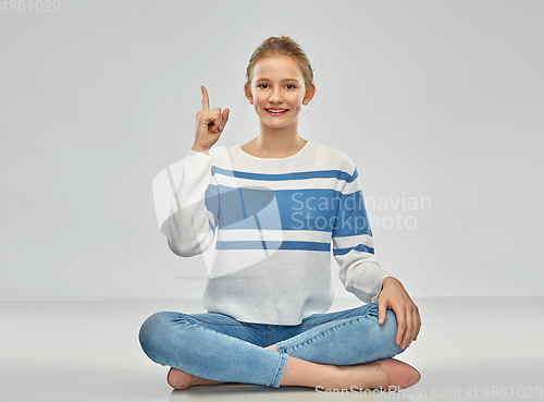 Image of teenage girl pointing finger up sitting on floor