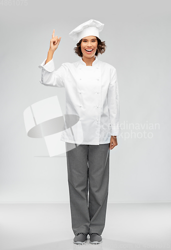 Image of smiling female chef in toque pointing finger up