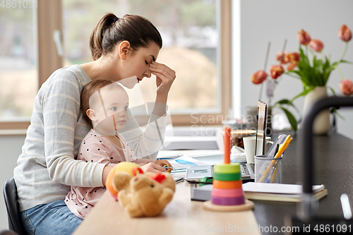 Image of tired mother with baby working at home office