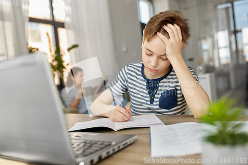 Image of student boy with book writing to notebook at home