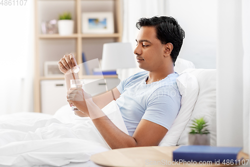 Image of man in bed dropping medicine into glass of water