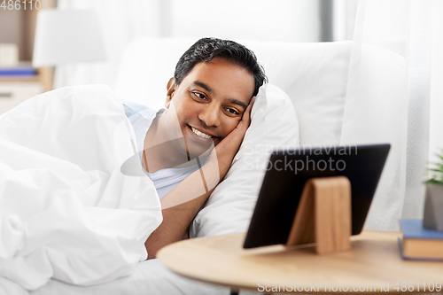 Image of happy indian man with tablet pc in bed at home