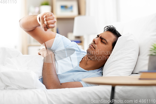 Image of indian man in bed looking at smart watch at home