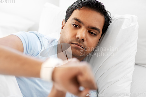 Image of indian man looking at smart watch in bed at home