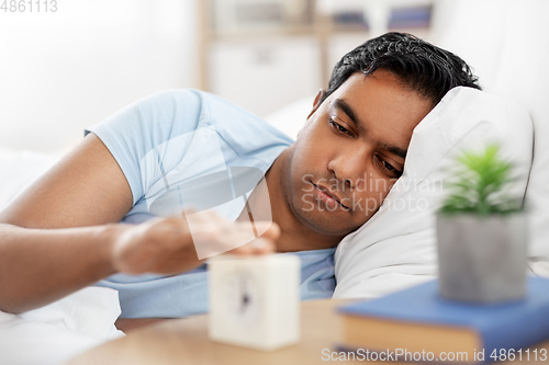 Image of indian man with alarm clock lying in bed