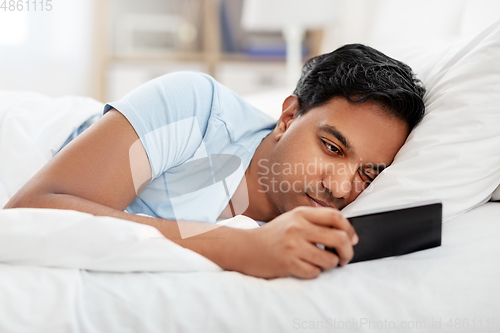 Image of sleepy indian man with smartphone lying in bed