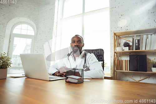 Image of African-american doctor consulting for patient, working in cabinet