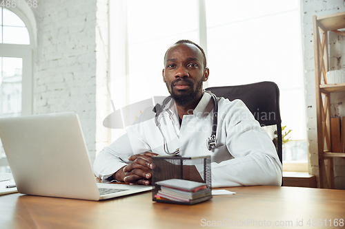 Image of African-american doctor consulting for patient, working in cabinet