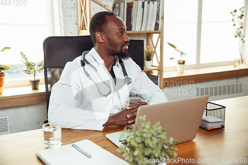 Image of African-american doctor consulting for patient, working in cabinet