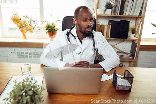 Image of African-american doctor consulting for patient, working in cabinet