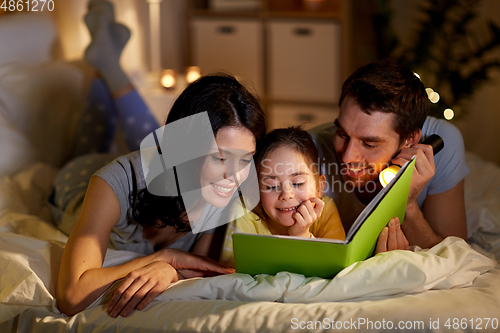 Image of happy family reading book in bed at night at home