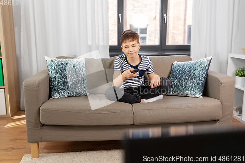 Image of bored boy with remote control watching tv at home