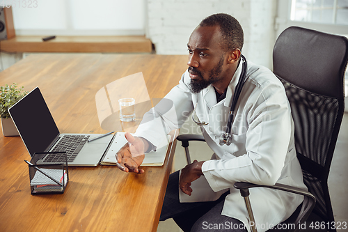 Image of African-american doctor consulting for patient, working in cabinet, close up