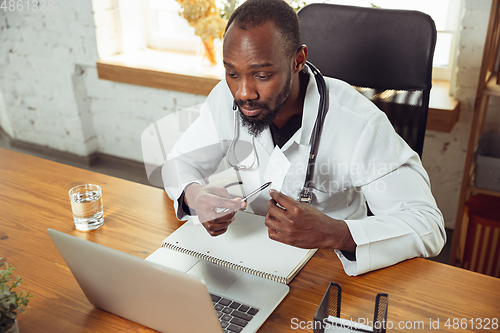 Image of African-american doctor consulting for patient, working in cabinet, close up