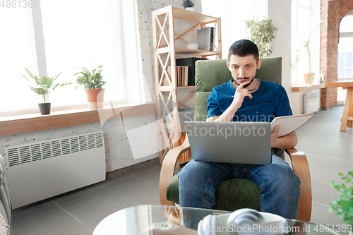 Image of Young focused man studying at home during online courses or free information by hisself