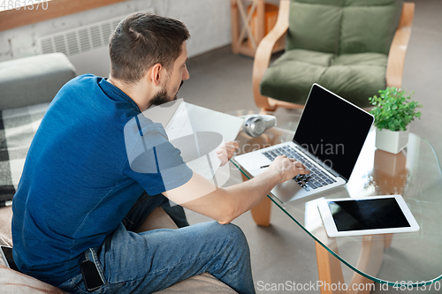 Image of Young focused man studying at home during online courses or free information by hisself