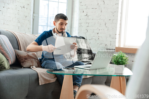 Image of Young focused man studying at home during online courses or free information by hisself