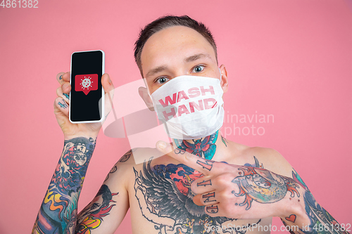 Image of Young man with freaky appearance on pink background wearing face mask with words WASH HANDS