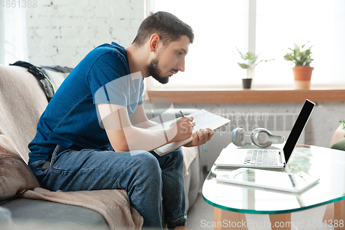 Image of Young focused man studying at home during online courses or free information by hisself