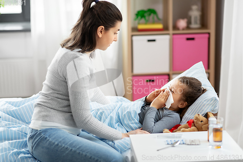 Image of mother and ill little daughter blowing nose in bed