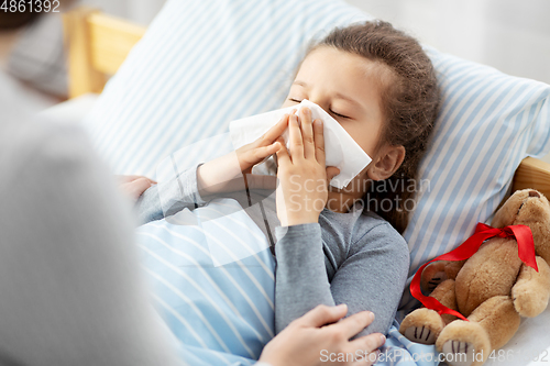 Image of mother and ill little daughter blowing nose in bed