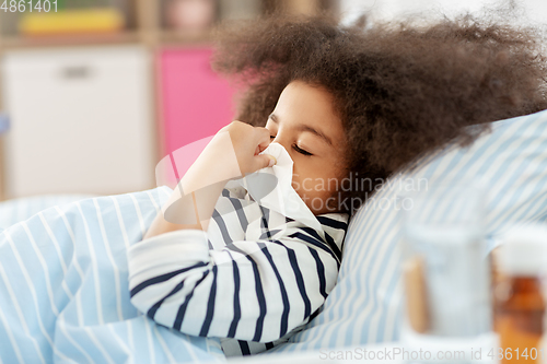 Image of sick girl lying in bed and blowing nose at home