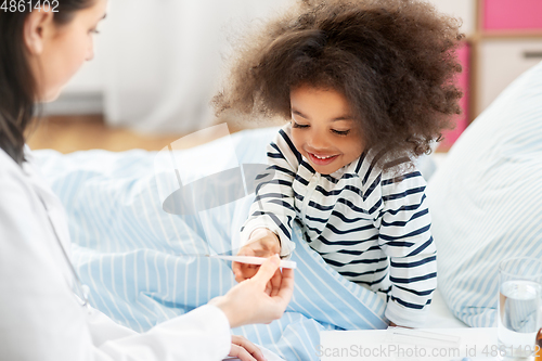 Image of doctor showing thermometer to smiling sick girl